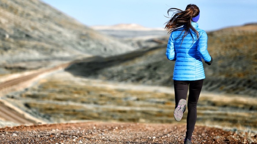 Frau joggt an einem Herbstmorgen über kiesige Hügel Frau joggt an einem Herbstmorgen über kiesige Hügel